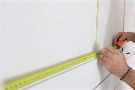 worker taking measurements on wall of home